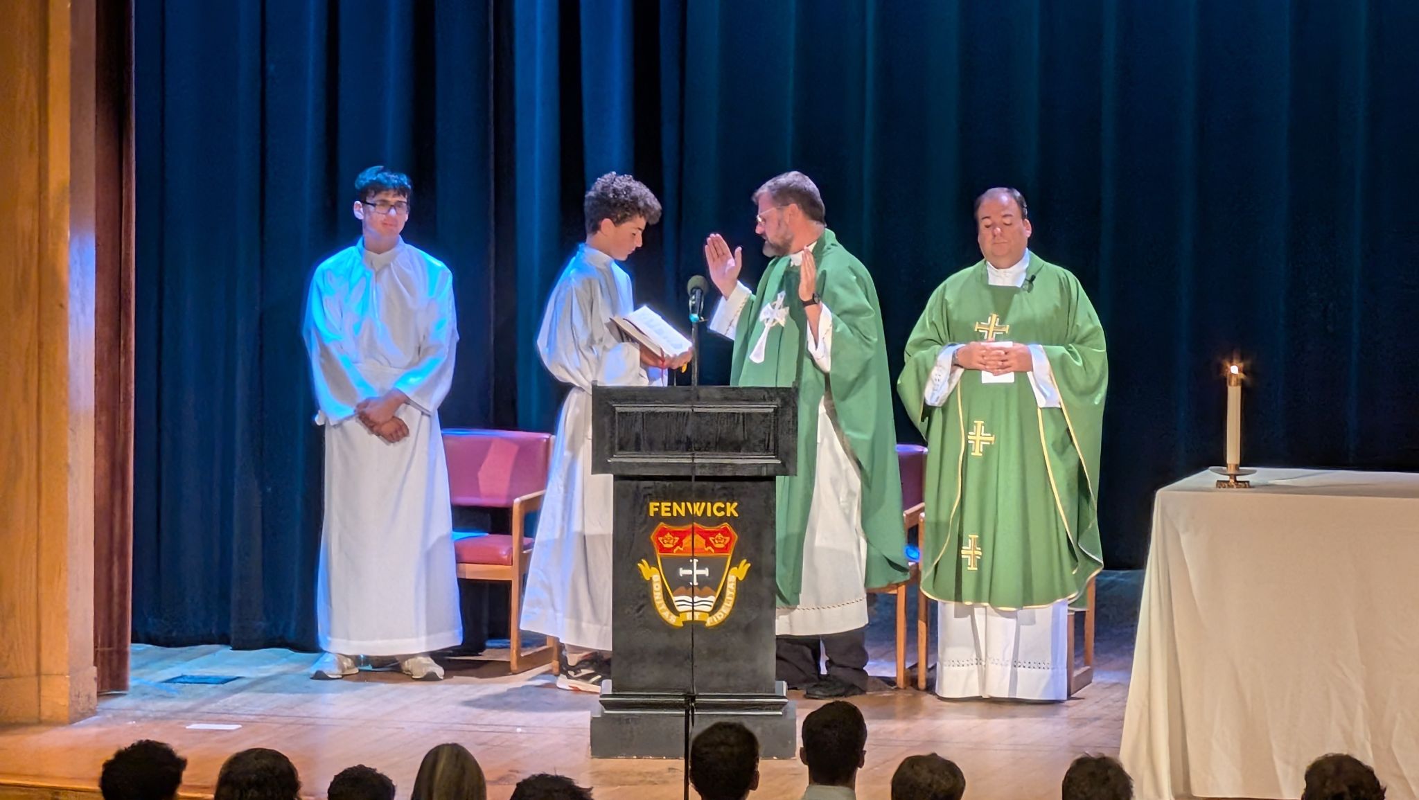 A Fenwick school Mass. Two priests and two altar servers stand at SR, behind a Fenwick podium.